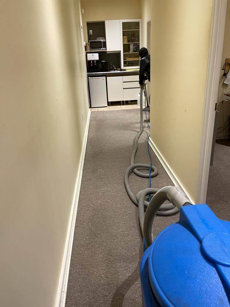 HR Property Maintenance (HRPM) technician using a high-powered extraction vacuum on a long hallway carpet in a Toronto office.