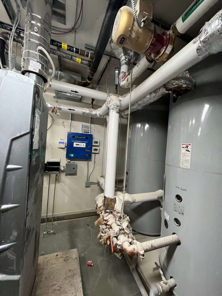 High-ceiling boiler room with heavy dust layer on pipes and tanks before HRPM cleaning.