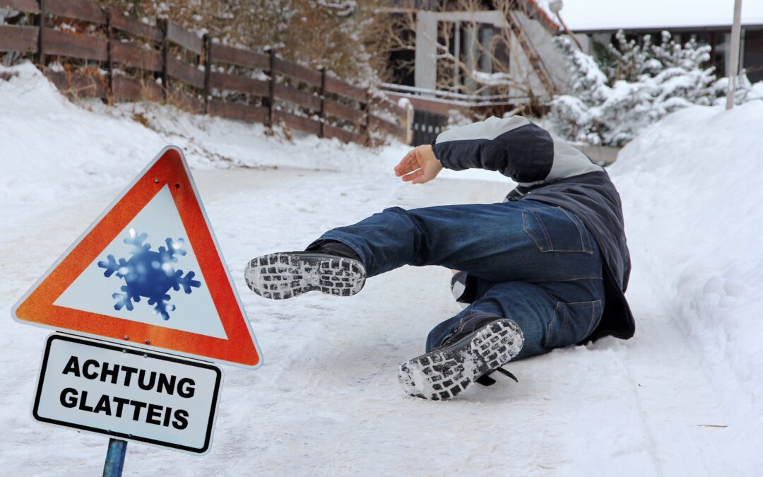 A person slipping and falling on an icy residential pathway in winter beside a warning sign for slippery ice.