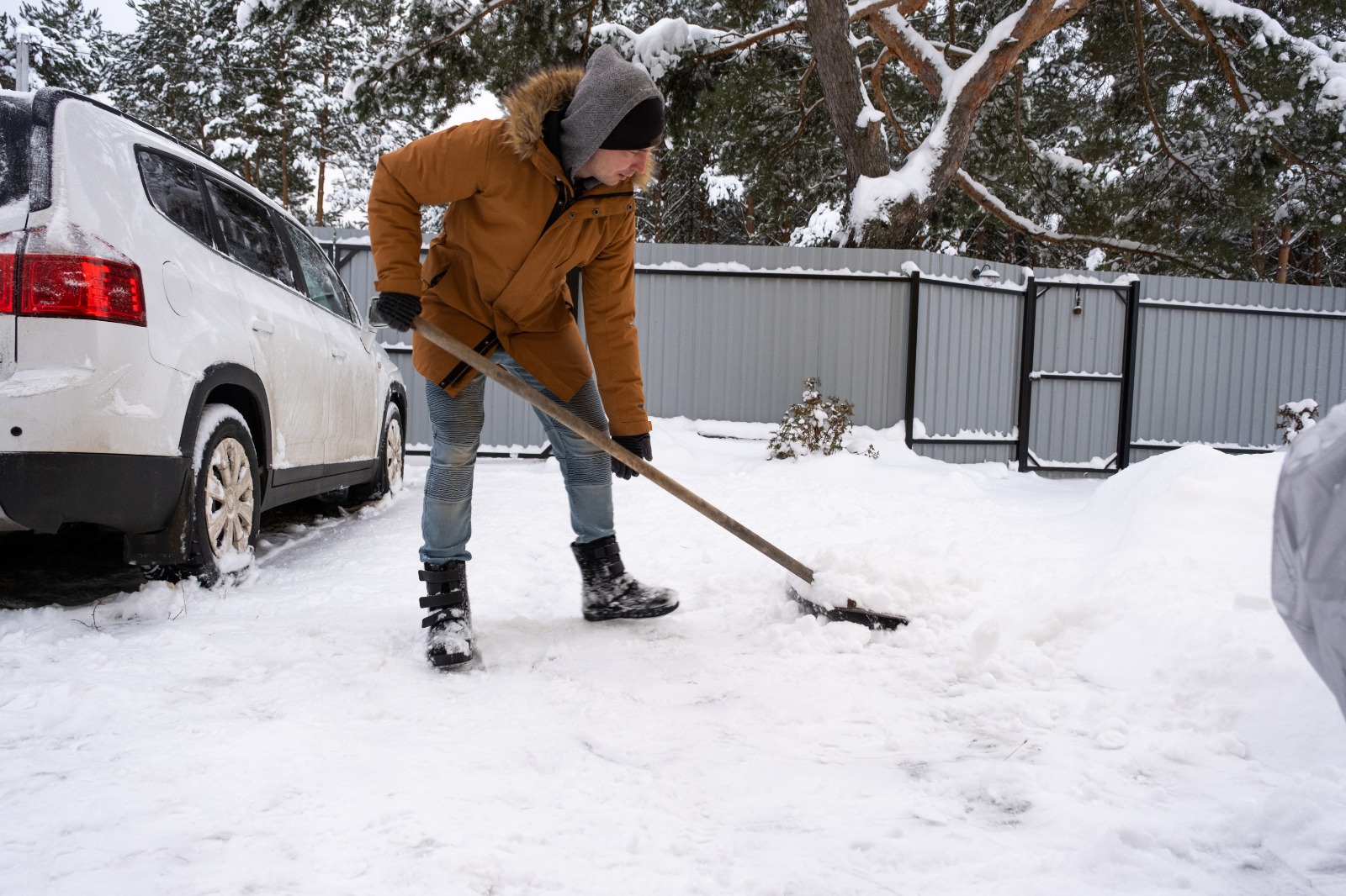 Property owner shoveling snow from a residential driveway beside a parked car during winter conditions.