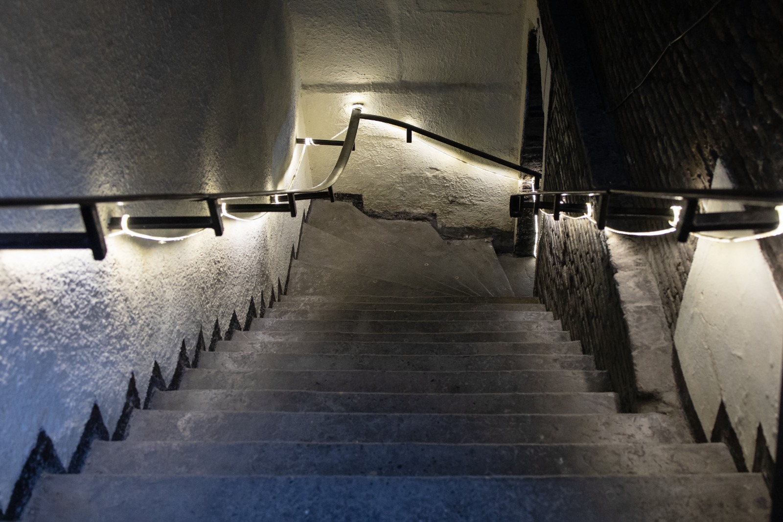 Dimly lit indoor stairwell with handrails and step-edge markings, highlighting a potential slip-and-fall hazard.