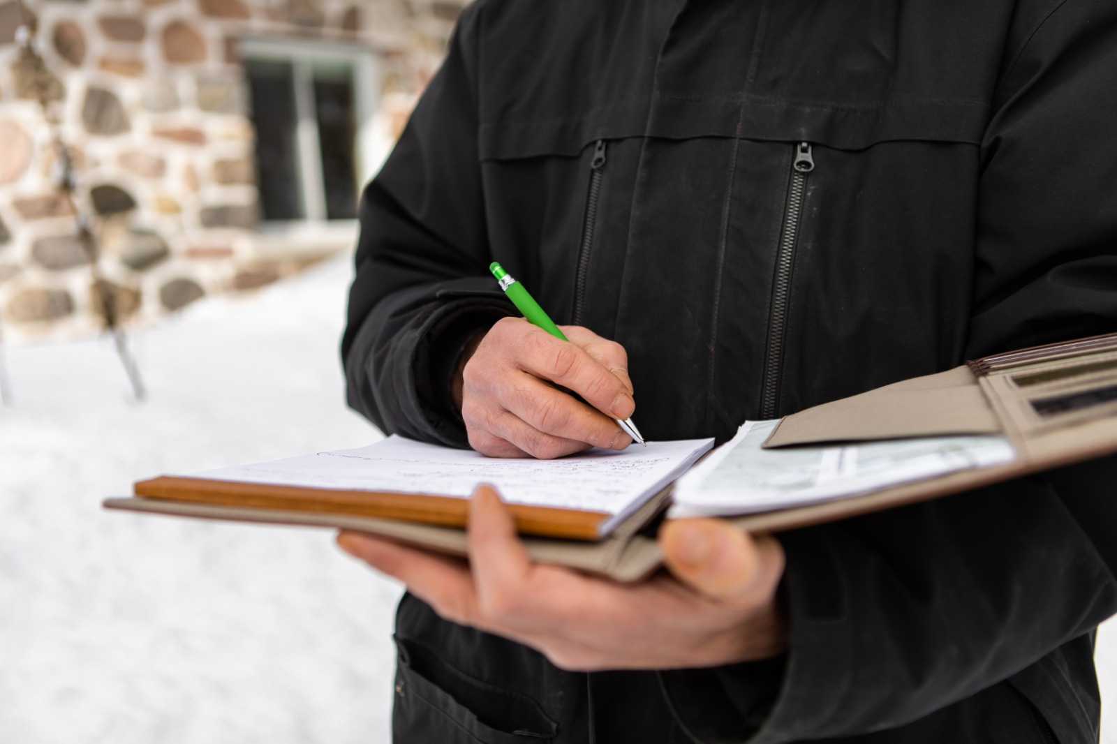 Property maintenance professional recording winter service details on a clipboard outdoors.